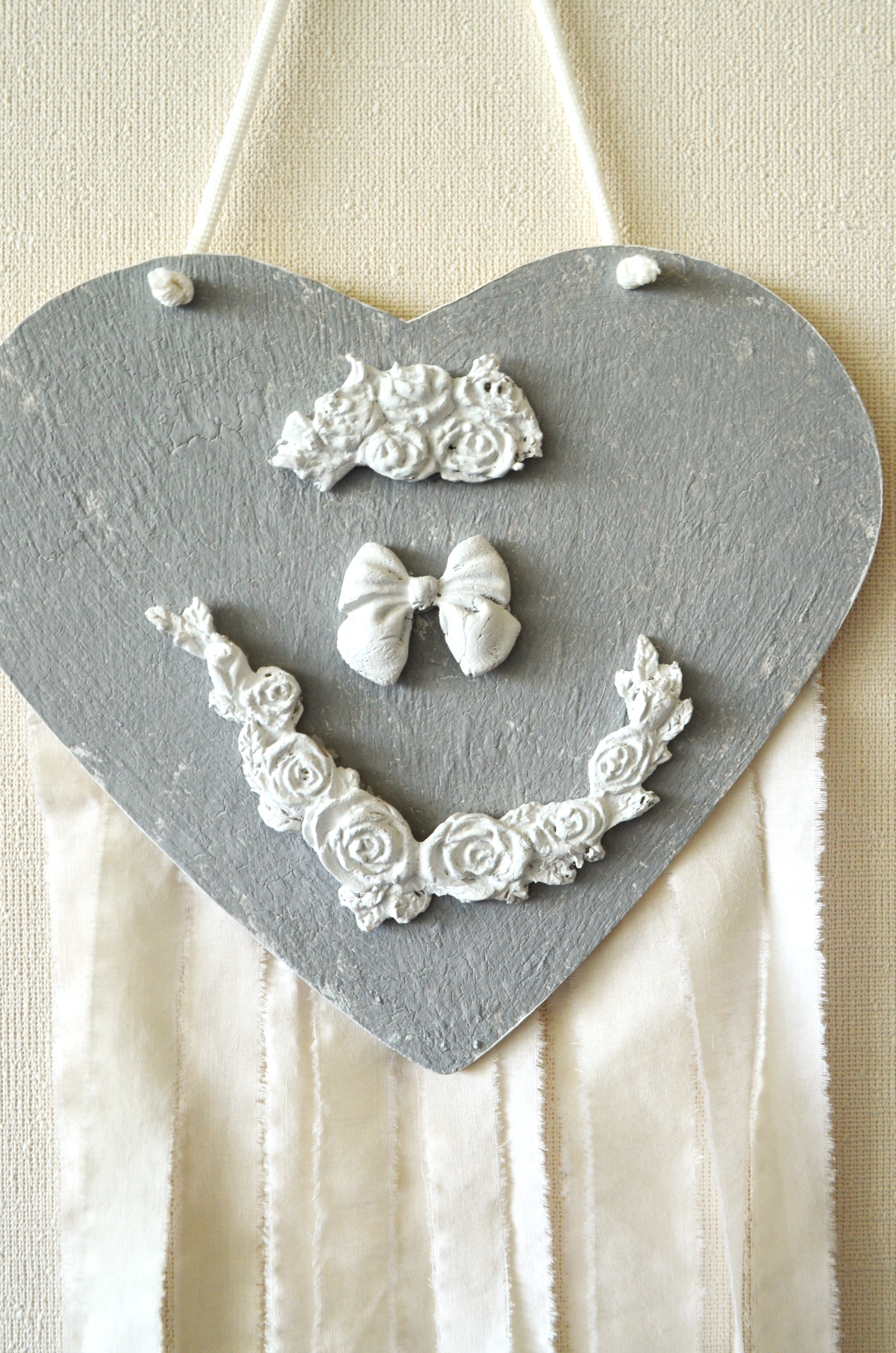 Detalle de adorno de pared infantil corazón gris estilo romántico con adornos en cerámicas y tiras de algodón exclusivo Lily Garden & deco