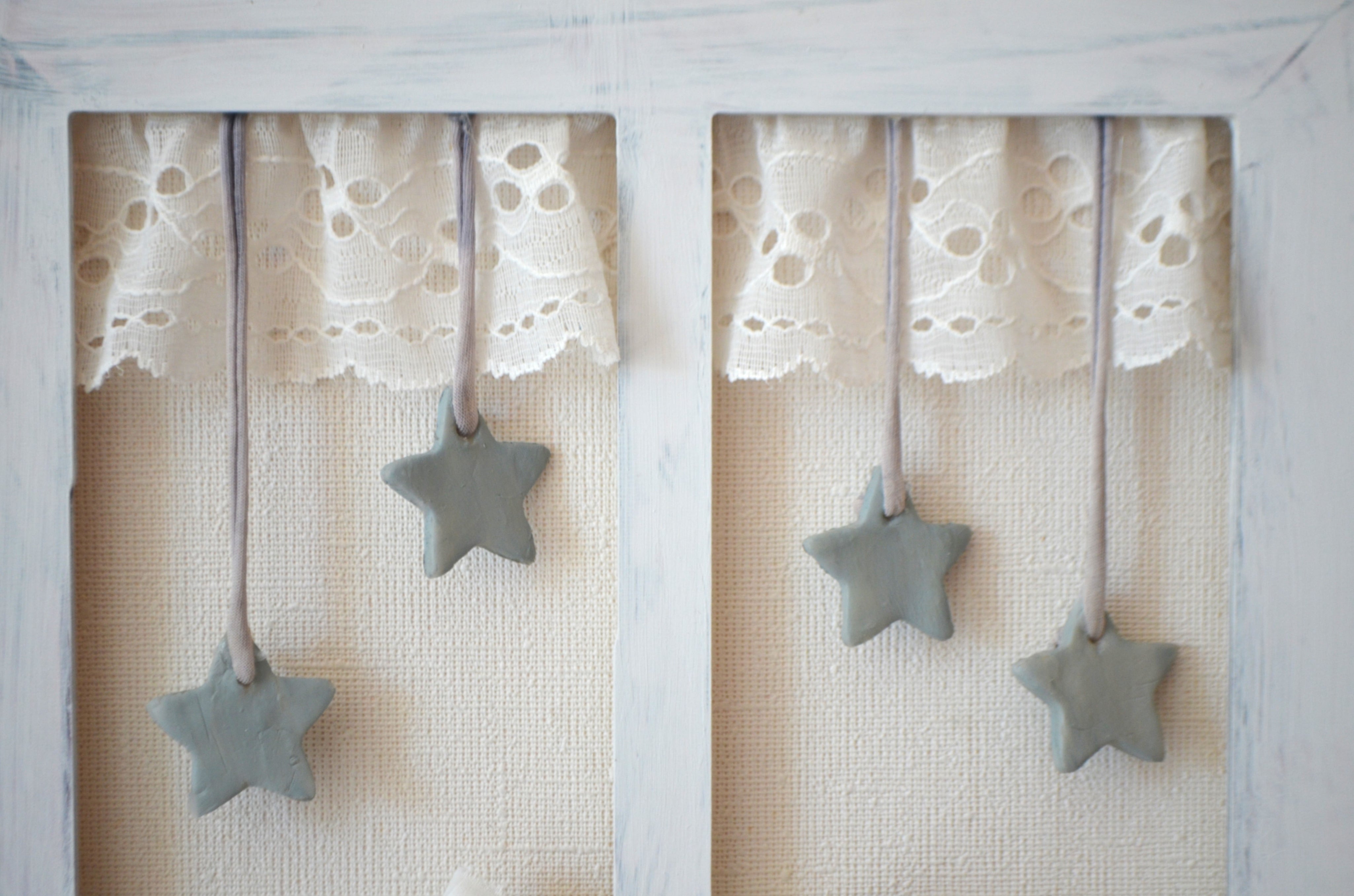 Detalle de cuadro de madera con forma de ventanita decorado con cortinas de encaje , estrellitas de cerámica y fibras naturales Exclusivo de Lily Garden & deco