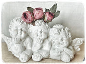 Figura religiosa que muestra  3 querubines decorados con flores preservadas Lily Garden & deco